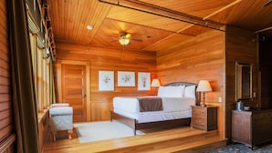 Une chambre aux murs lambrissés, avec un lit, des tables de chevet et un ventilateur de plafond.