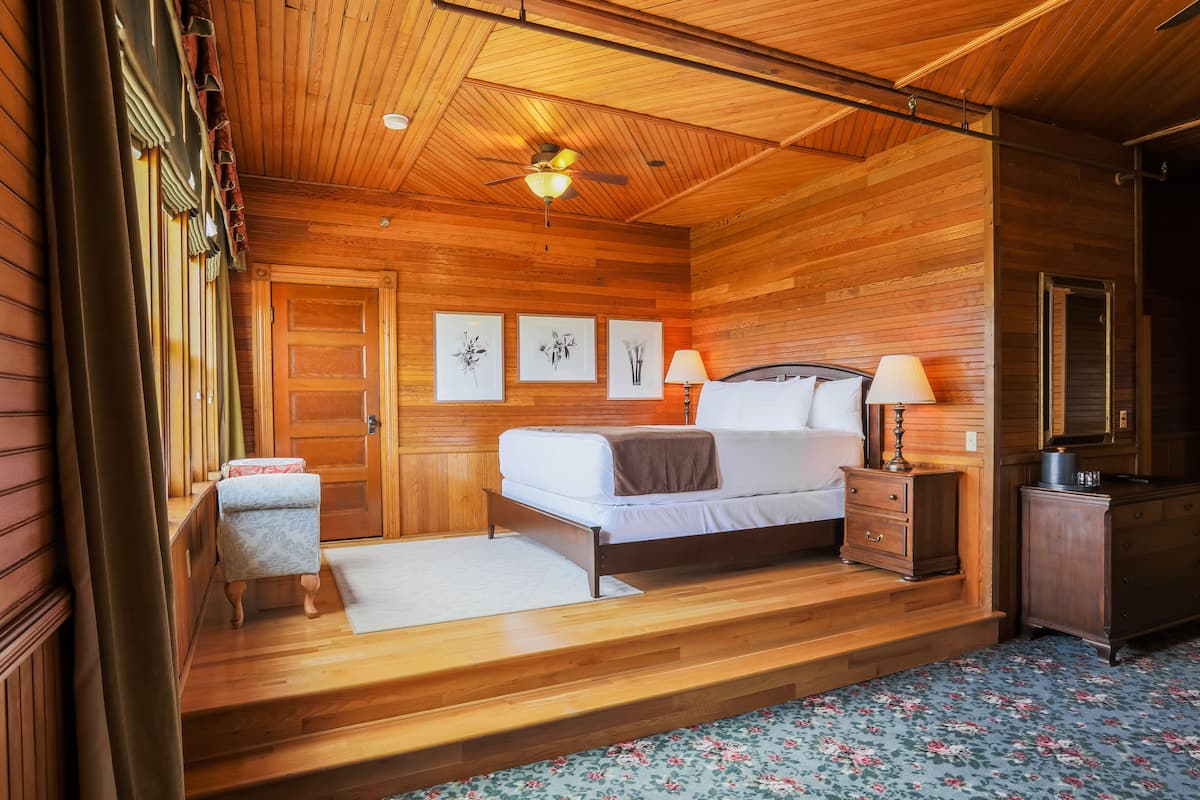 Une chambre aux murs lambrissés, avec un lit, des tables de chevet et un ventilateur de plafond.