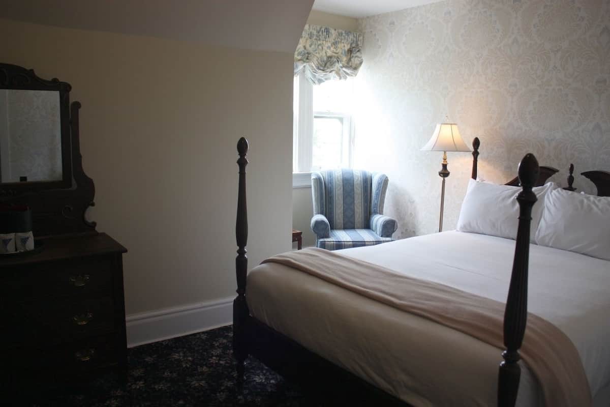 Une chambre à coucher avec un lit à baldaquin, une chaise, une commode et une fenêtre avec des rideaux.