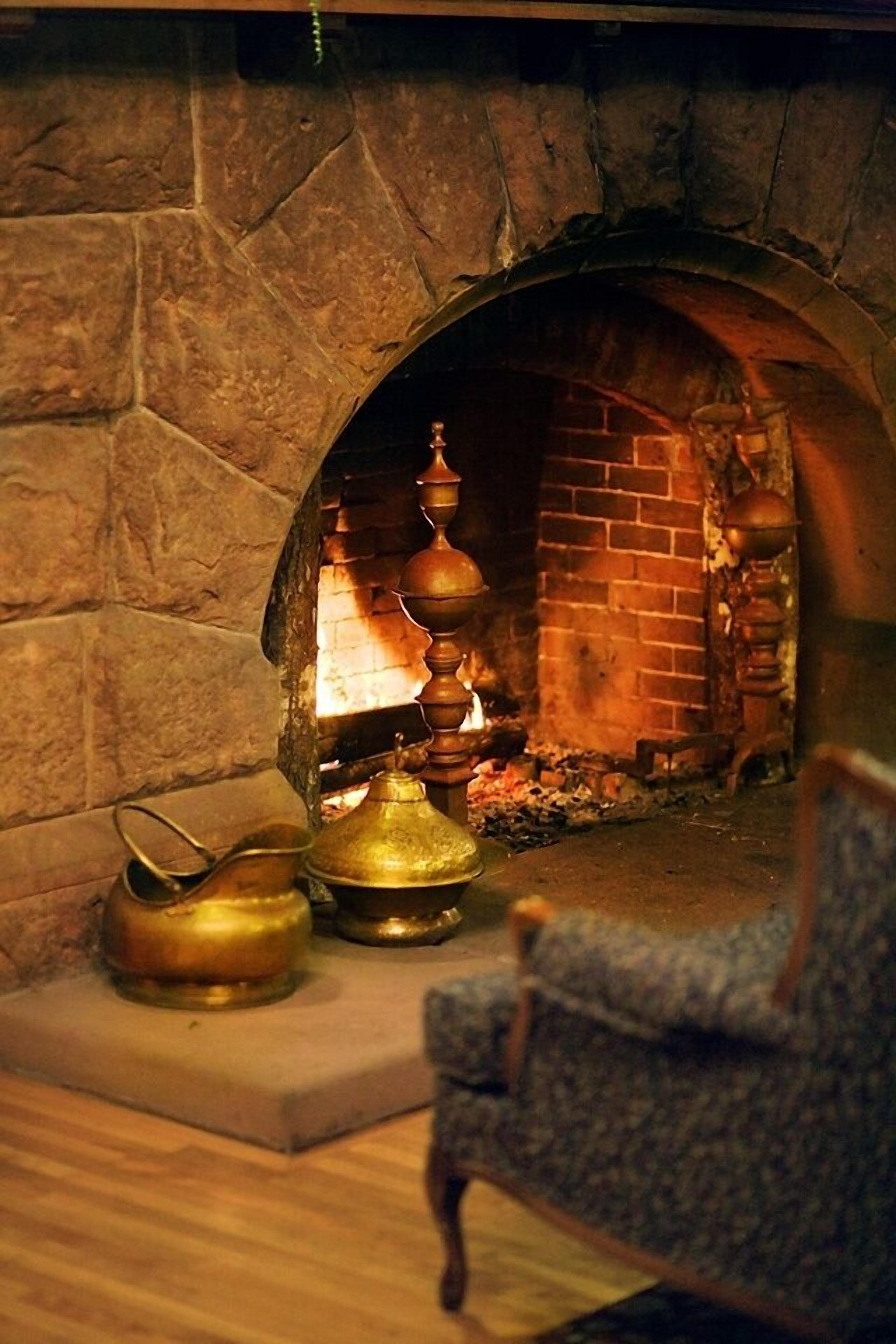 A stone fireplace with a brick interior, a traditional tea set, and a chair in front.