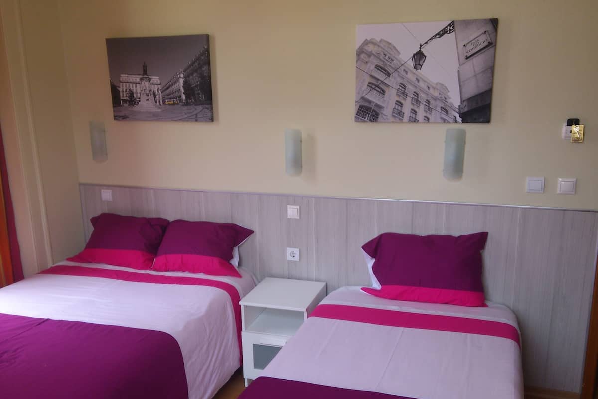 A hotel room with two beds, each with a white and pink bedspread, and two wall-mounted nightstands. There are two framed pictures on the wall above the beds.