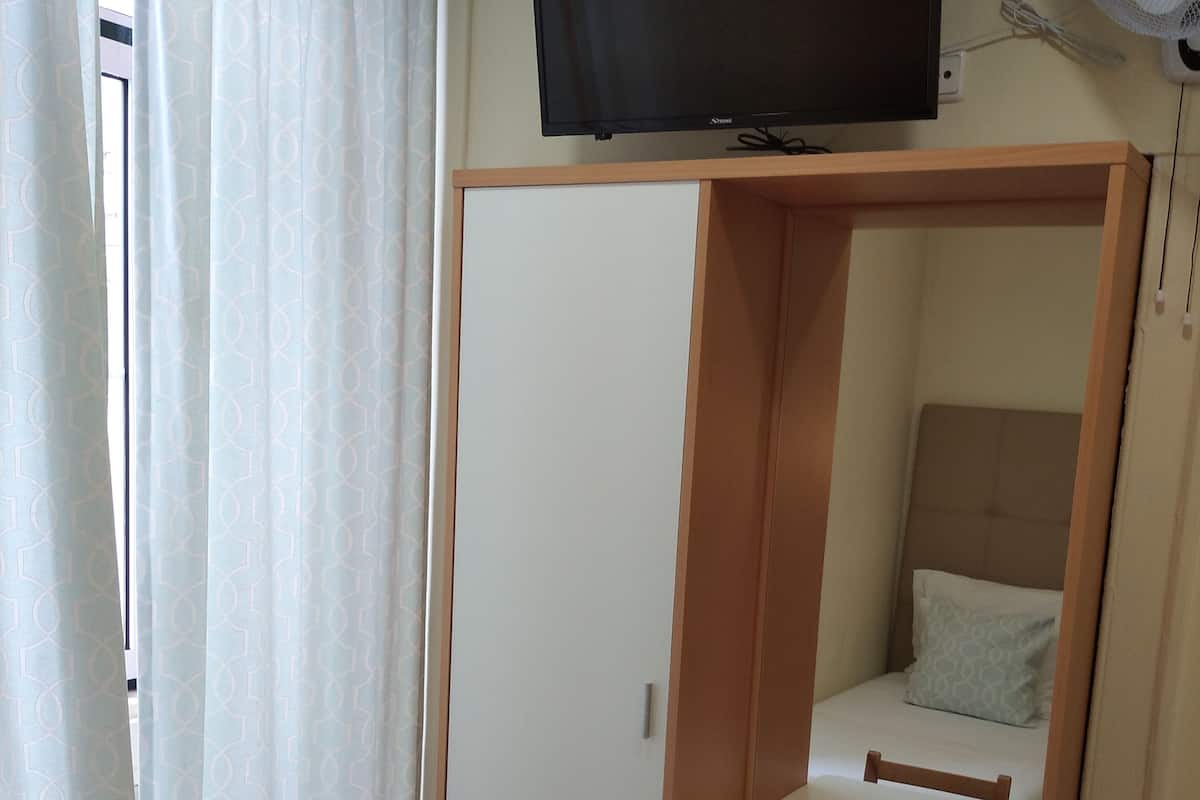 A compact room with a bed, a desk, and a TV mounted on the wall.