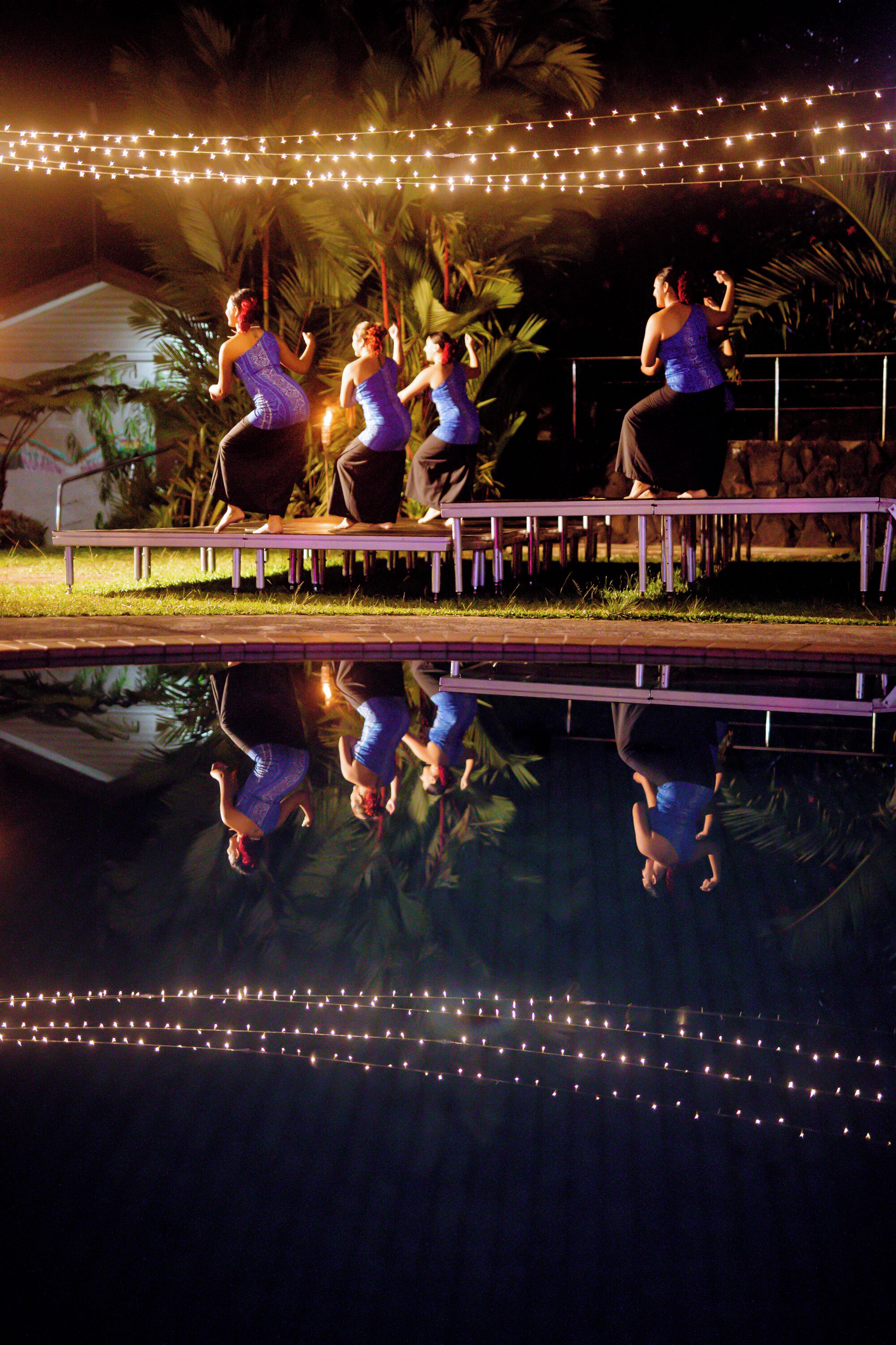 A pool with string lights above and reflections of people on the water's surface.
