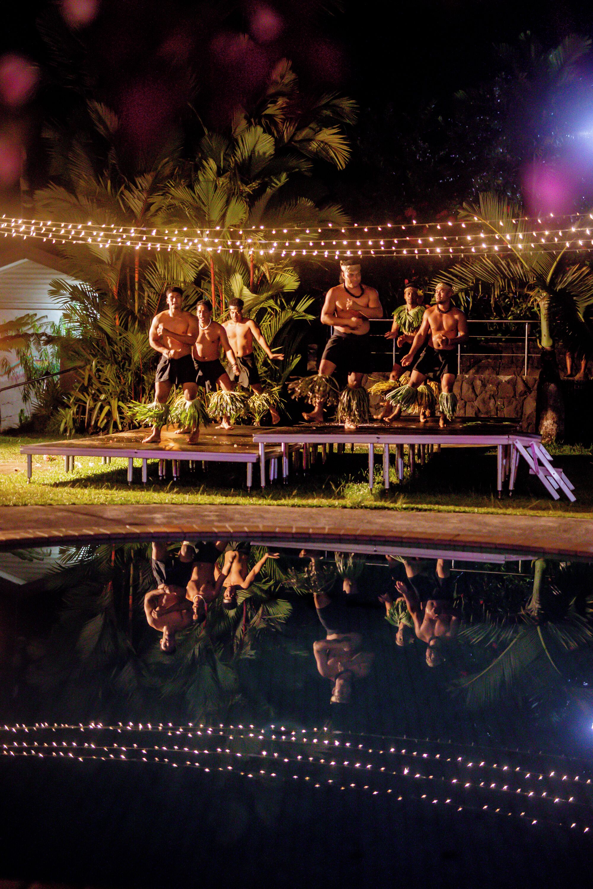 A stage with performers in tropical attire, surrounded by palm trees and string lights.