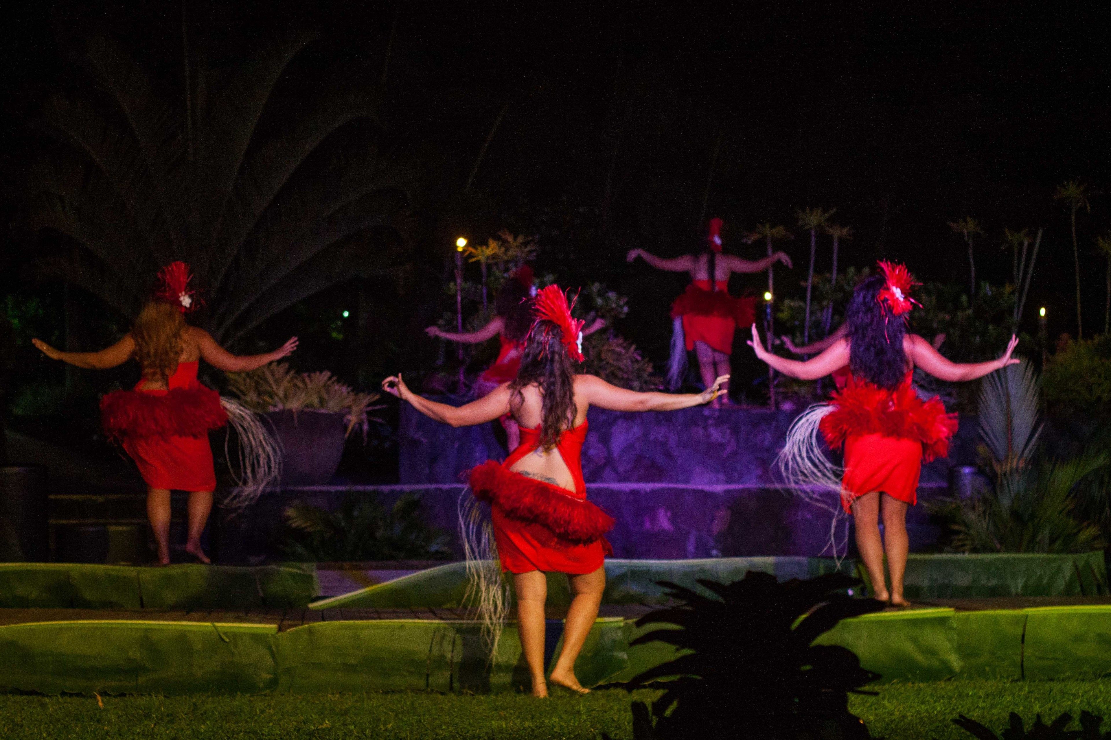 Espetáculo noturno ao ar livre com dançarinos vestidos de vermelho.