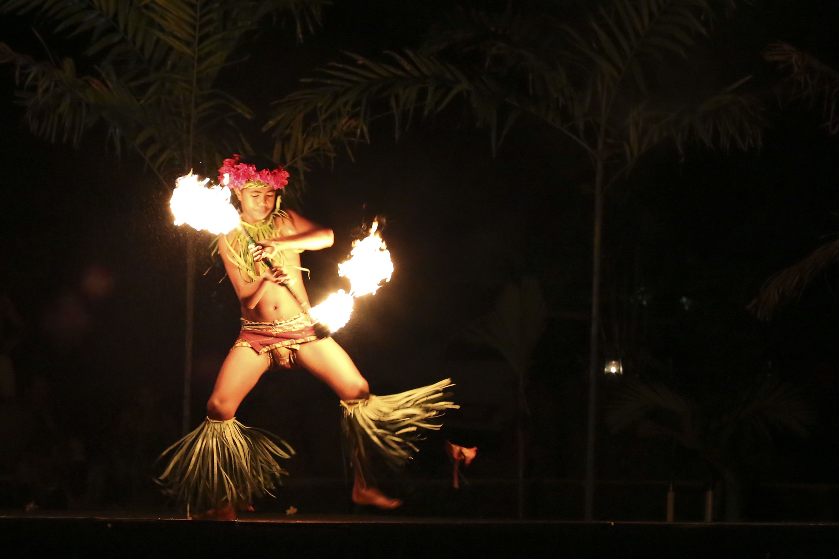 A performer with fire props in a tropical setting.