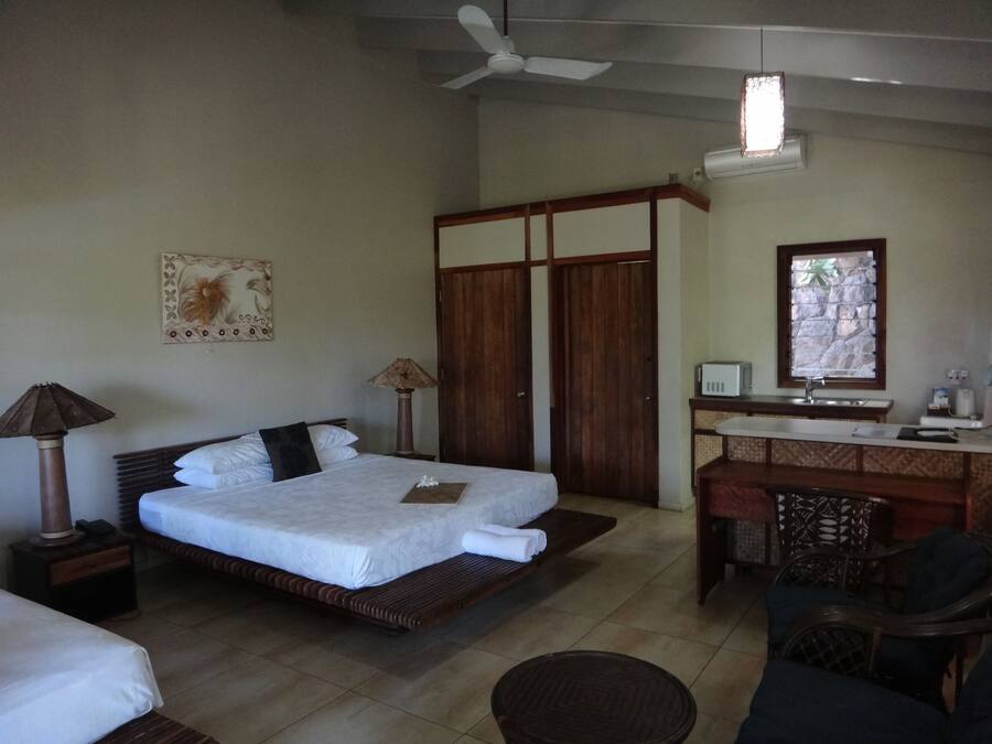 A bedroom with a bed, a desk, a chair, a lamp, a ceiling fan, and a window.