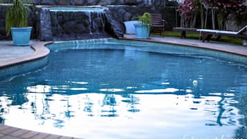 Una piscina con cascada, rodeada de plantas en macetas y un banco.