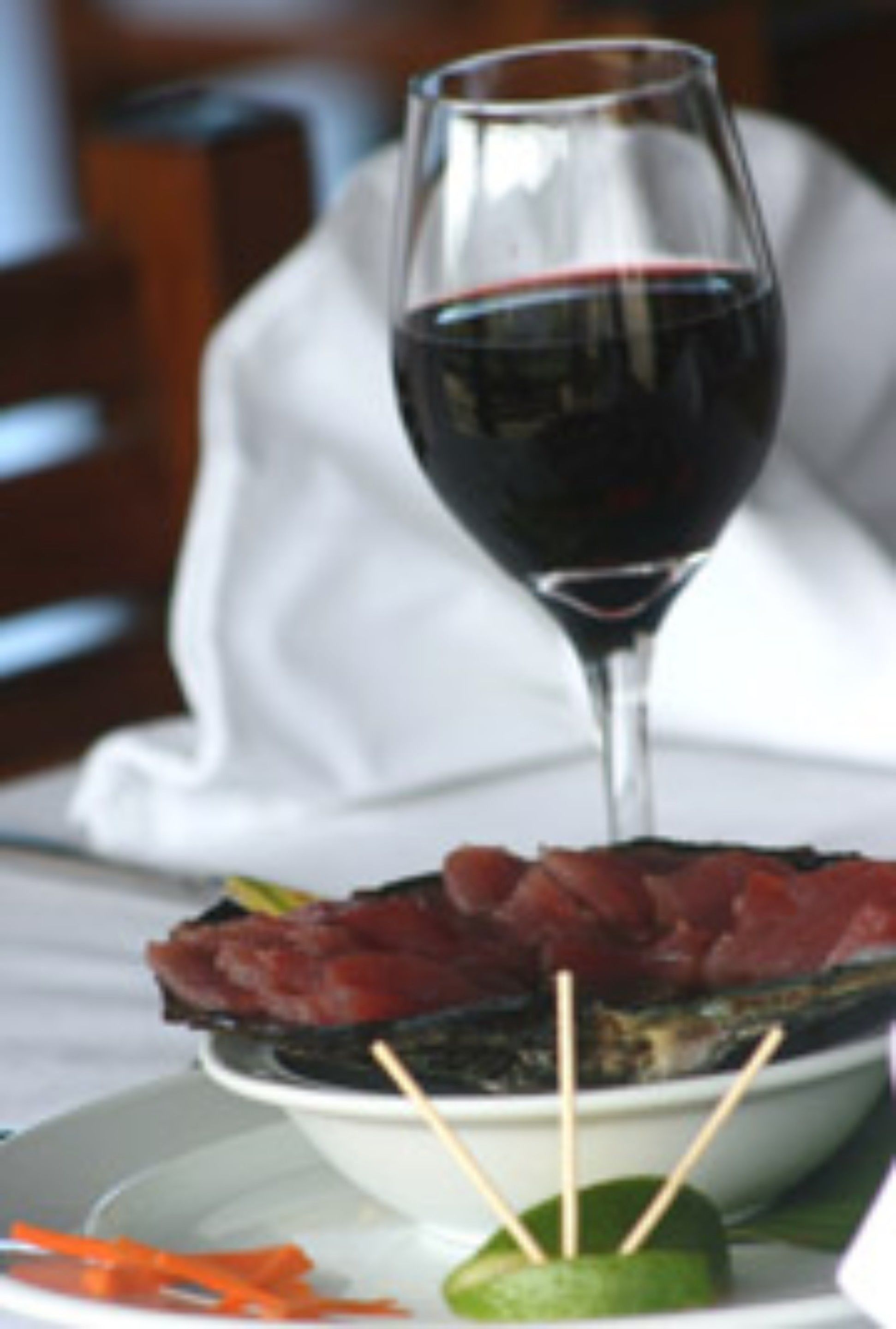 A glass of red wine on a table with a plate of food, including meat and vegetables.