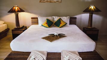 Un lit bien fait, avec du linge de lit blanc, deux coussins décoratifs, un petit set de table en fibres tressées et deux serviettes ornées de motifs floraux.