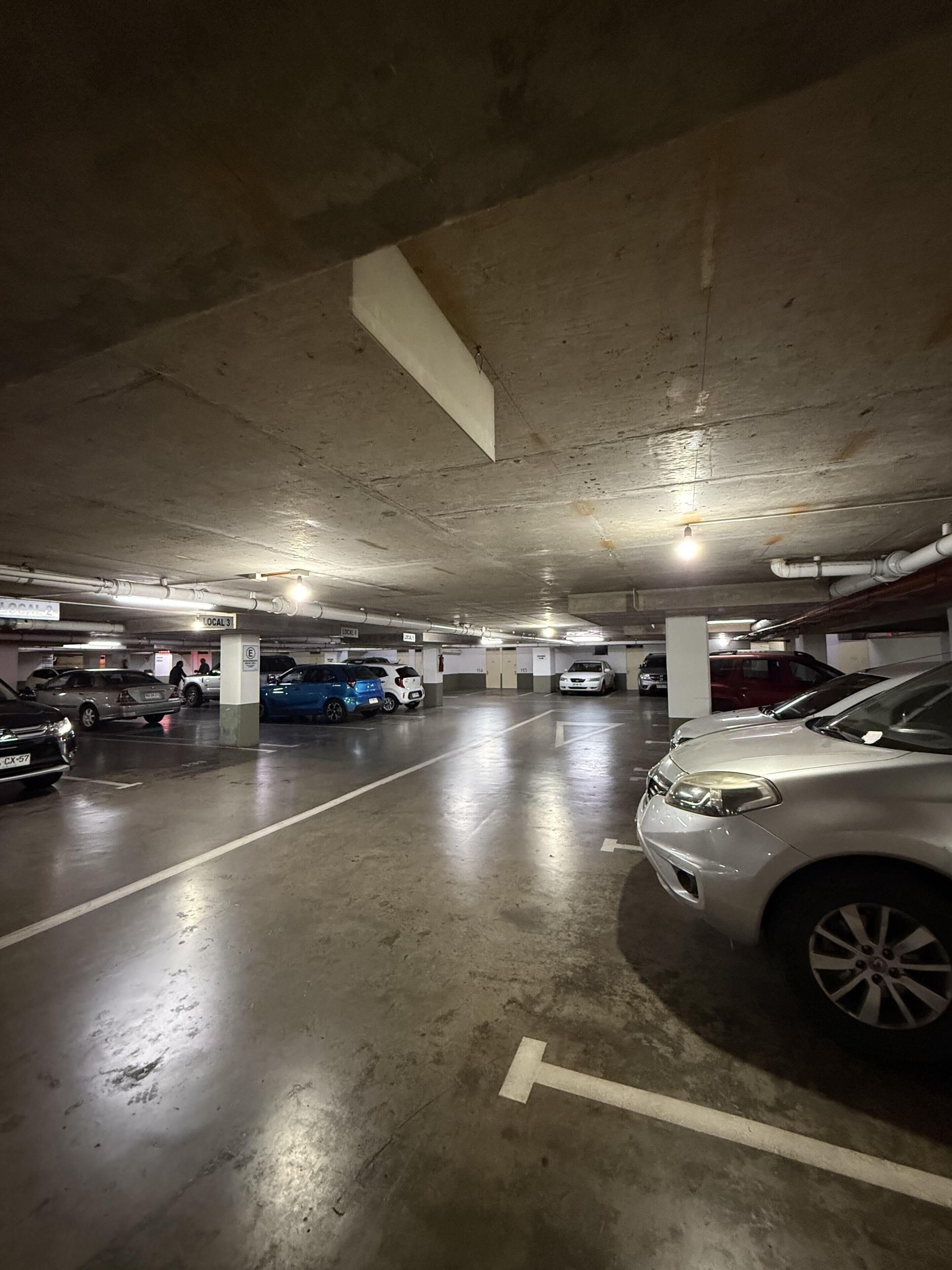 Un parking souterrain à plusieurs niveaux, doté de planchers et de murs en béton, de places de stationnement délimitées et d’un éclairage au plafond.