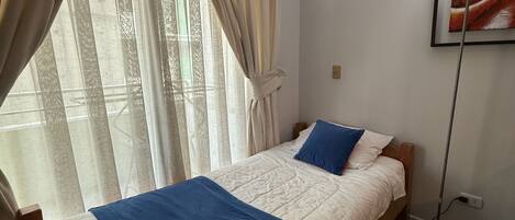 Una cama individual con una colcha azul y naranja, un cabecero de madera y una pared blanca con un cuadro enmarcado.