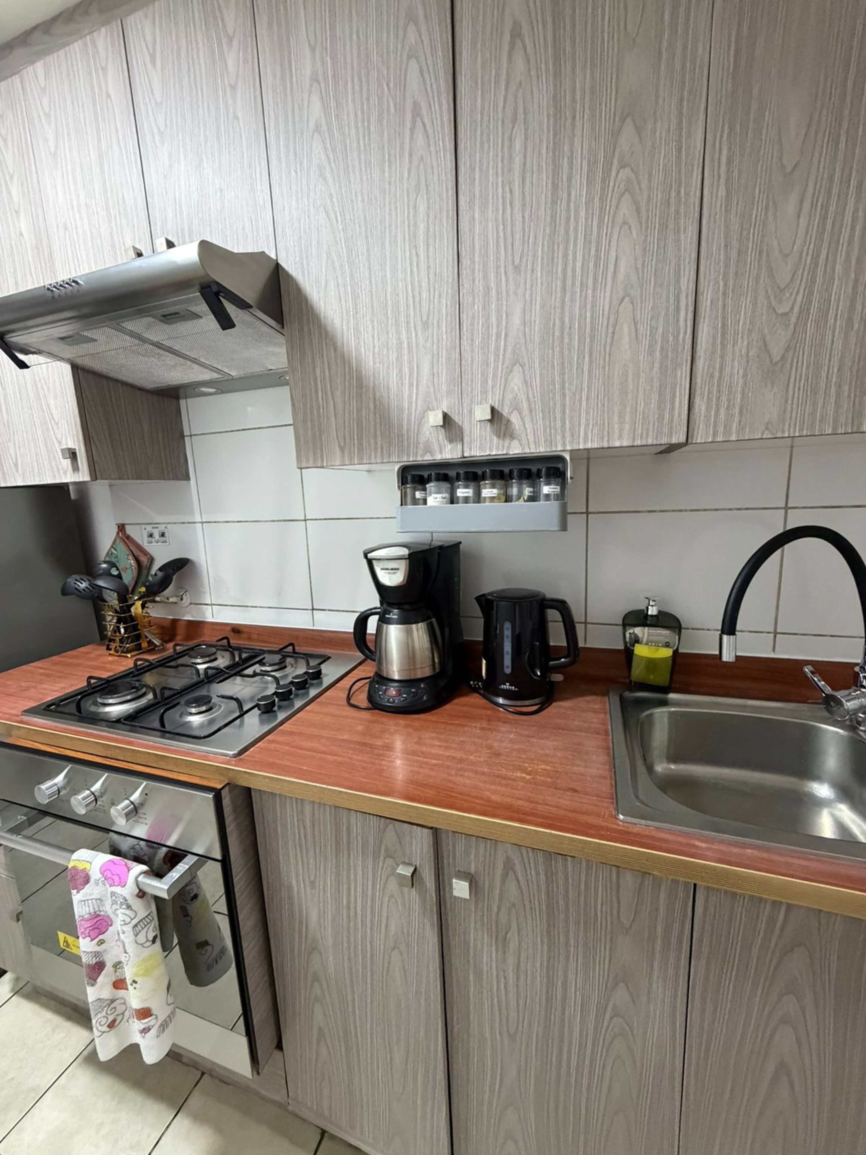 A kitchen with a gas stove, coffee maker, kettle, and a built-in spice rack.