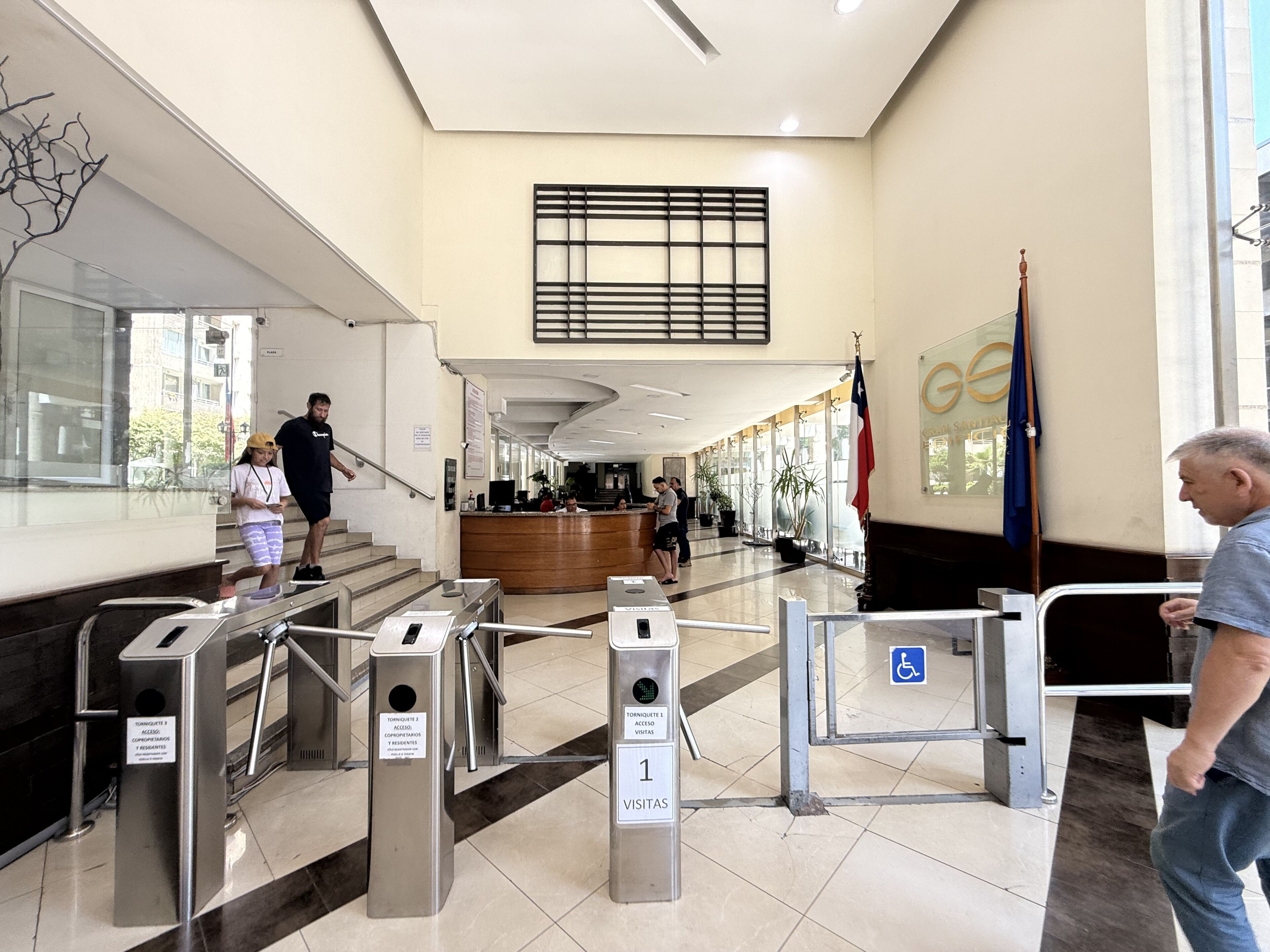 Un vestíbulo con mostrador de recepción, escalera y torniquete con señalización de acceso para visitantes.