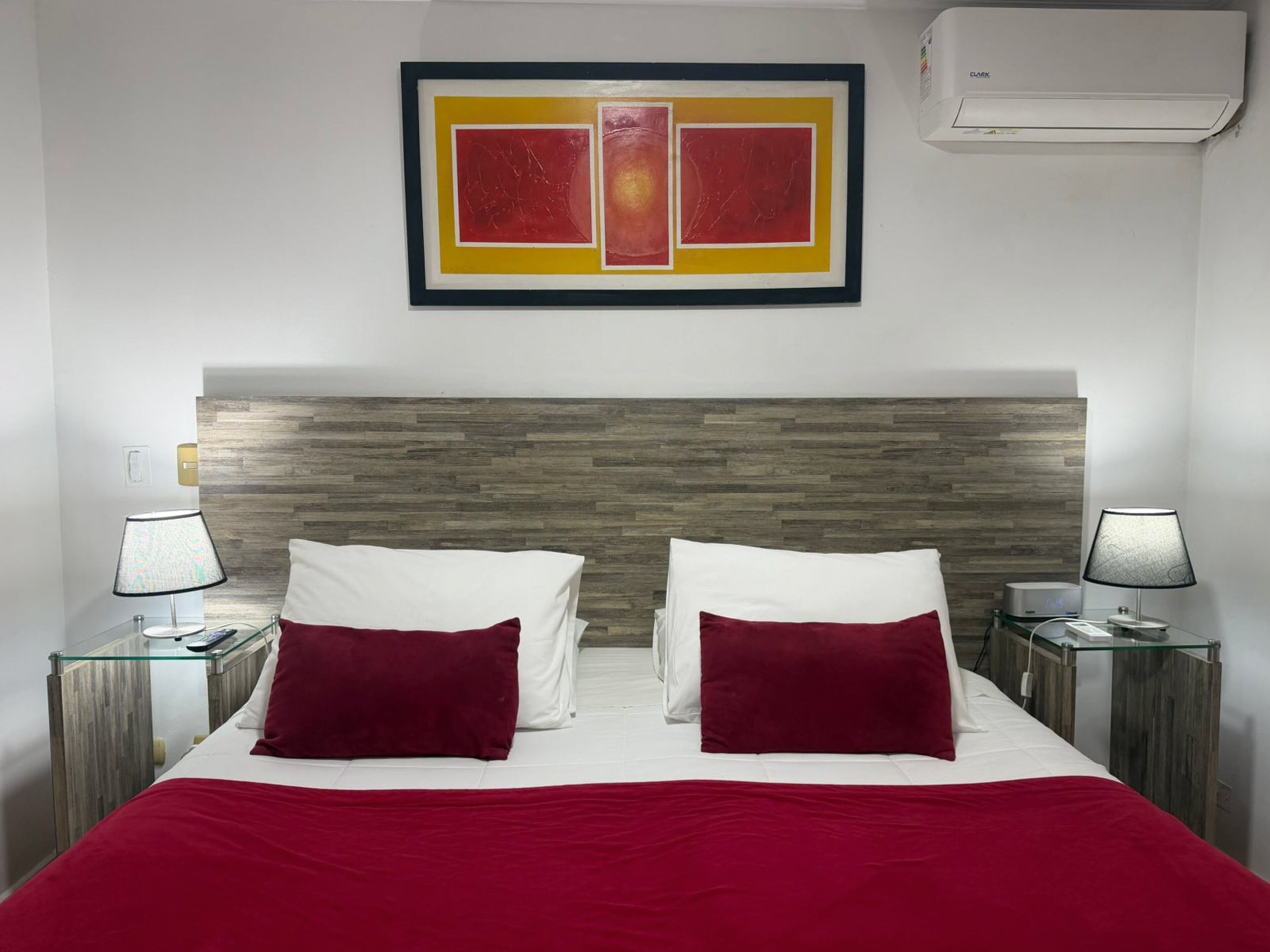 Una camera d'albergo con un letto, due comodini, lampade, un quadro incorniciato e un condizionatore d'aria.