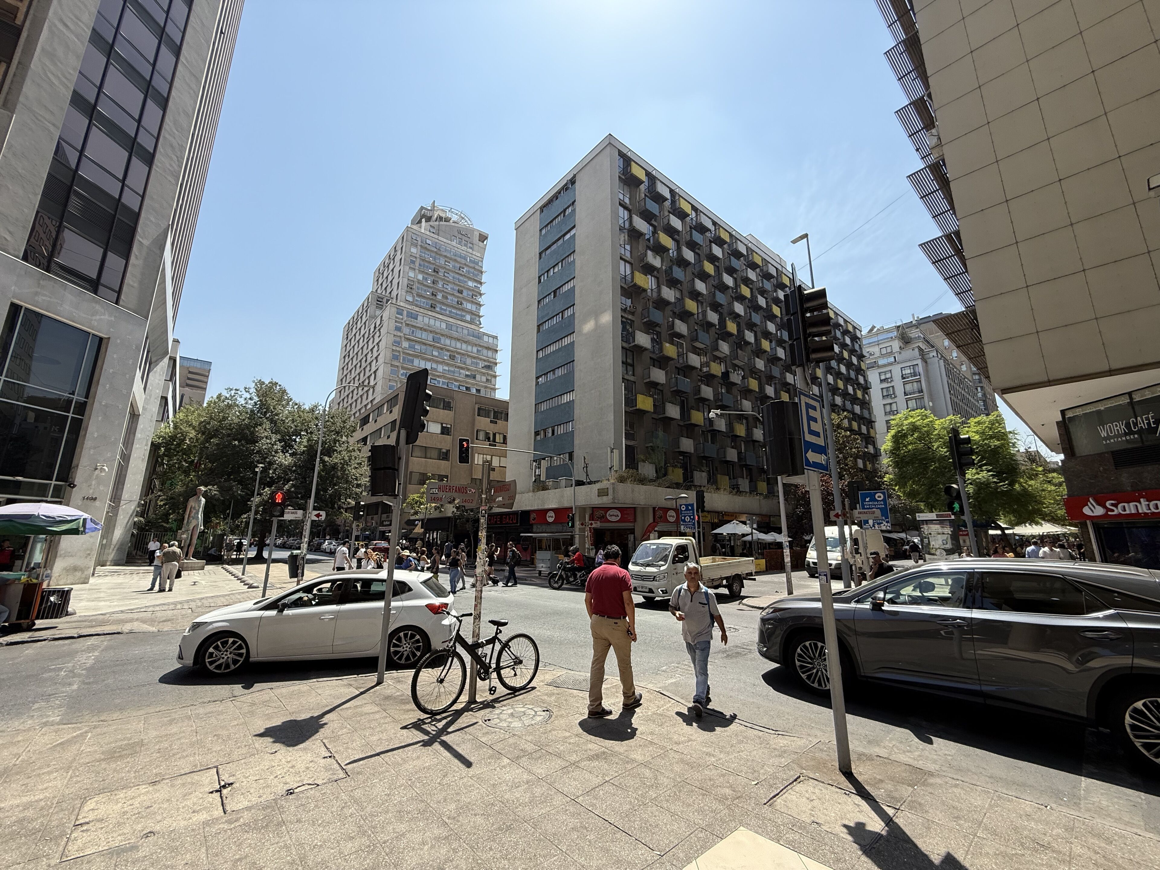 A busy urban street with tall buildings, a traffic light, and a bicycle parked on the sidewalk.