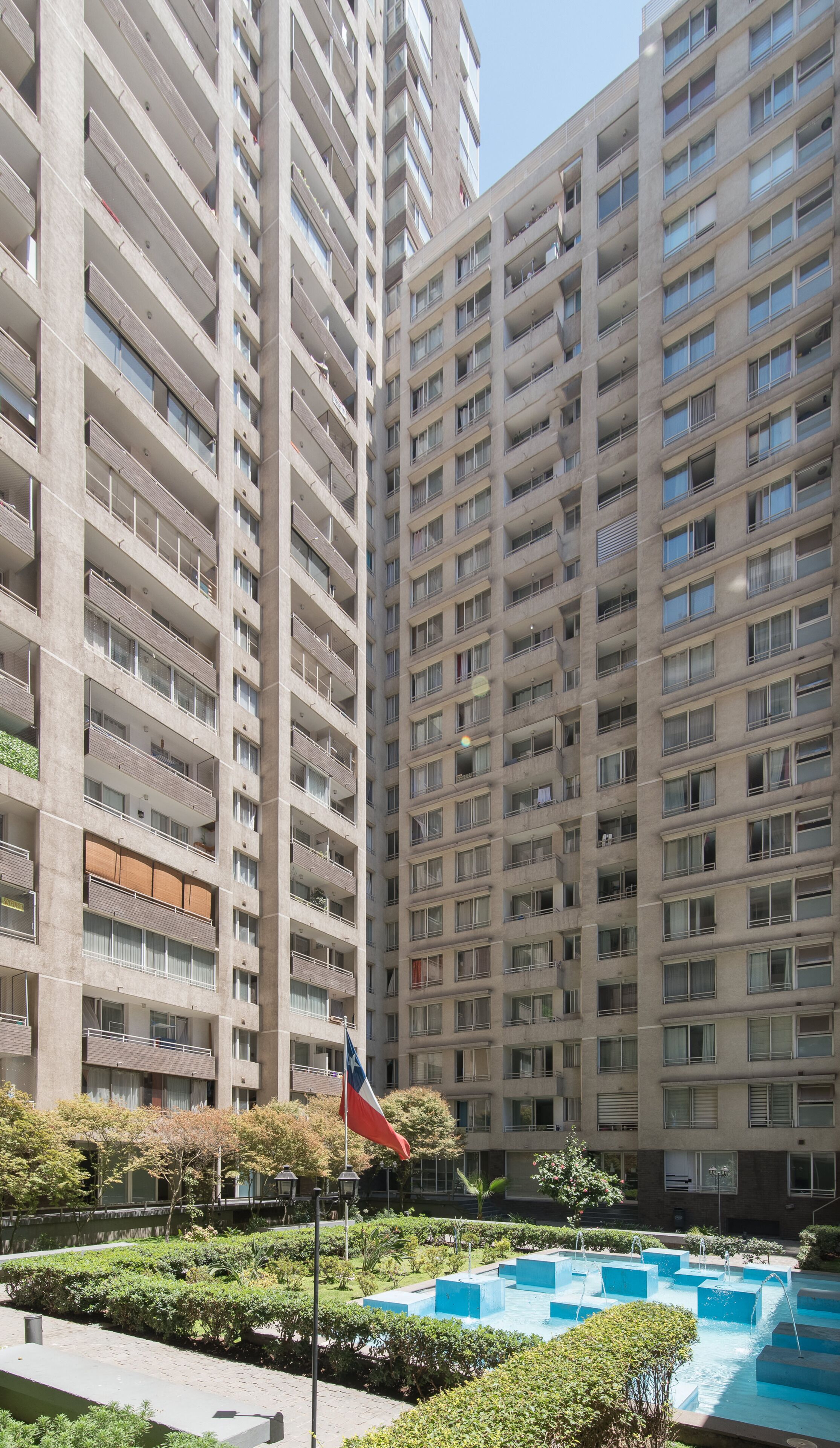 A high-rise residential building with multiple balconies, a flag, and a water feature.