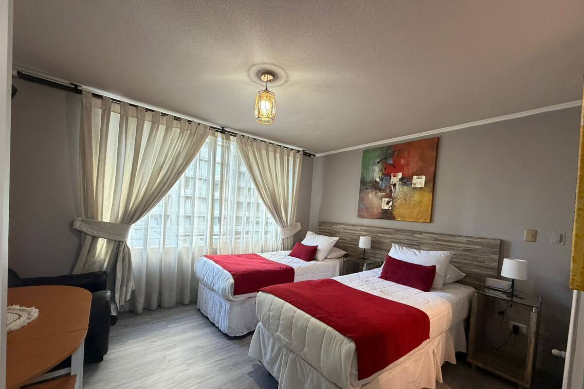 Una habitación de hotel con dos camas, un escritorio, una silla, una mesita de noche y un cuadro en la pared.