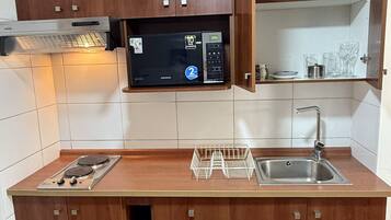 A compact kitchen with wooden cabinets, a microwave, a sink, and a dish rack.