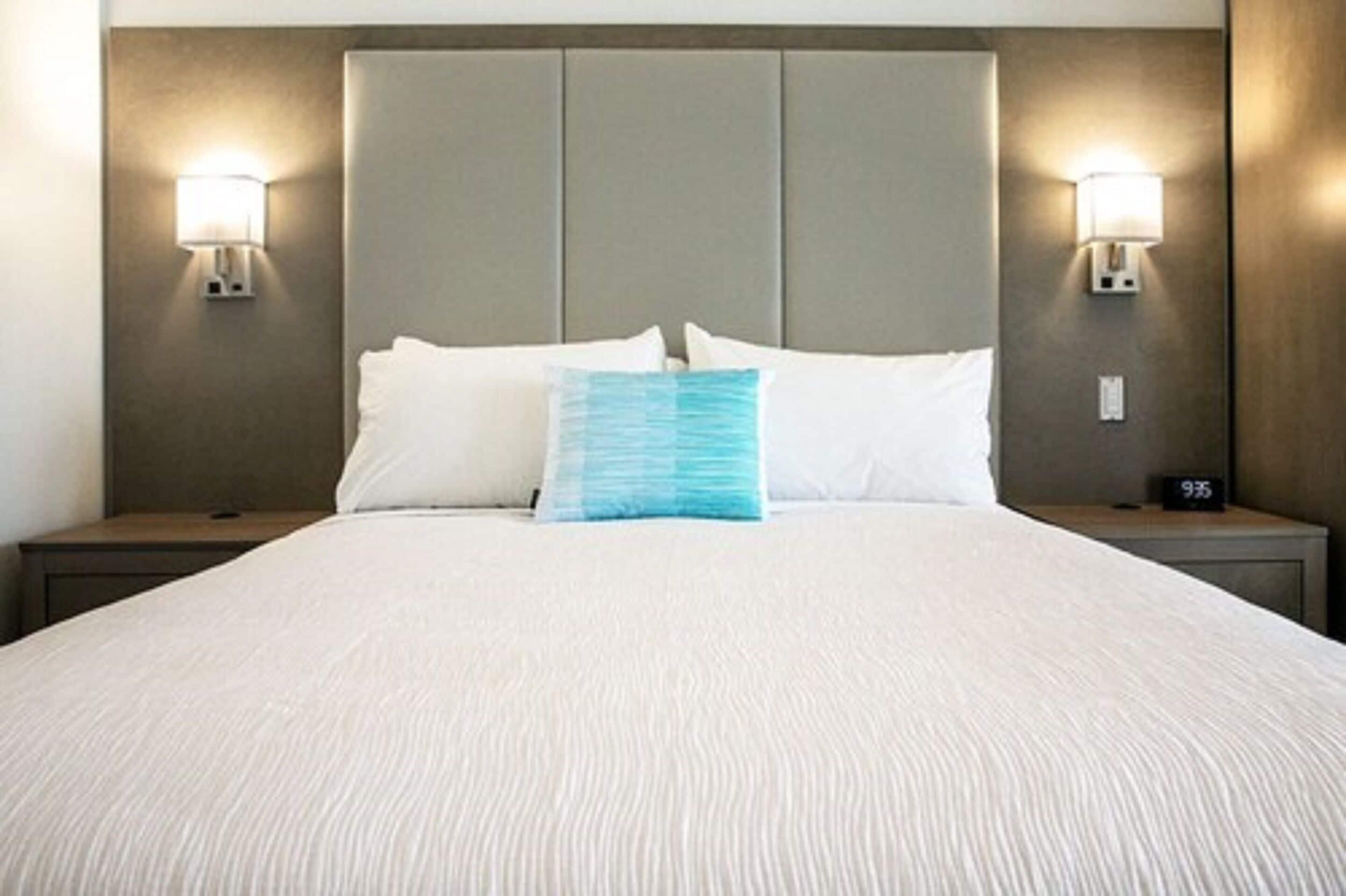 A neatly made bed with a white and blue pillow, two bedside lamps, and a nightstand with a clock.