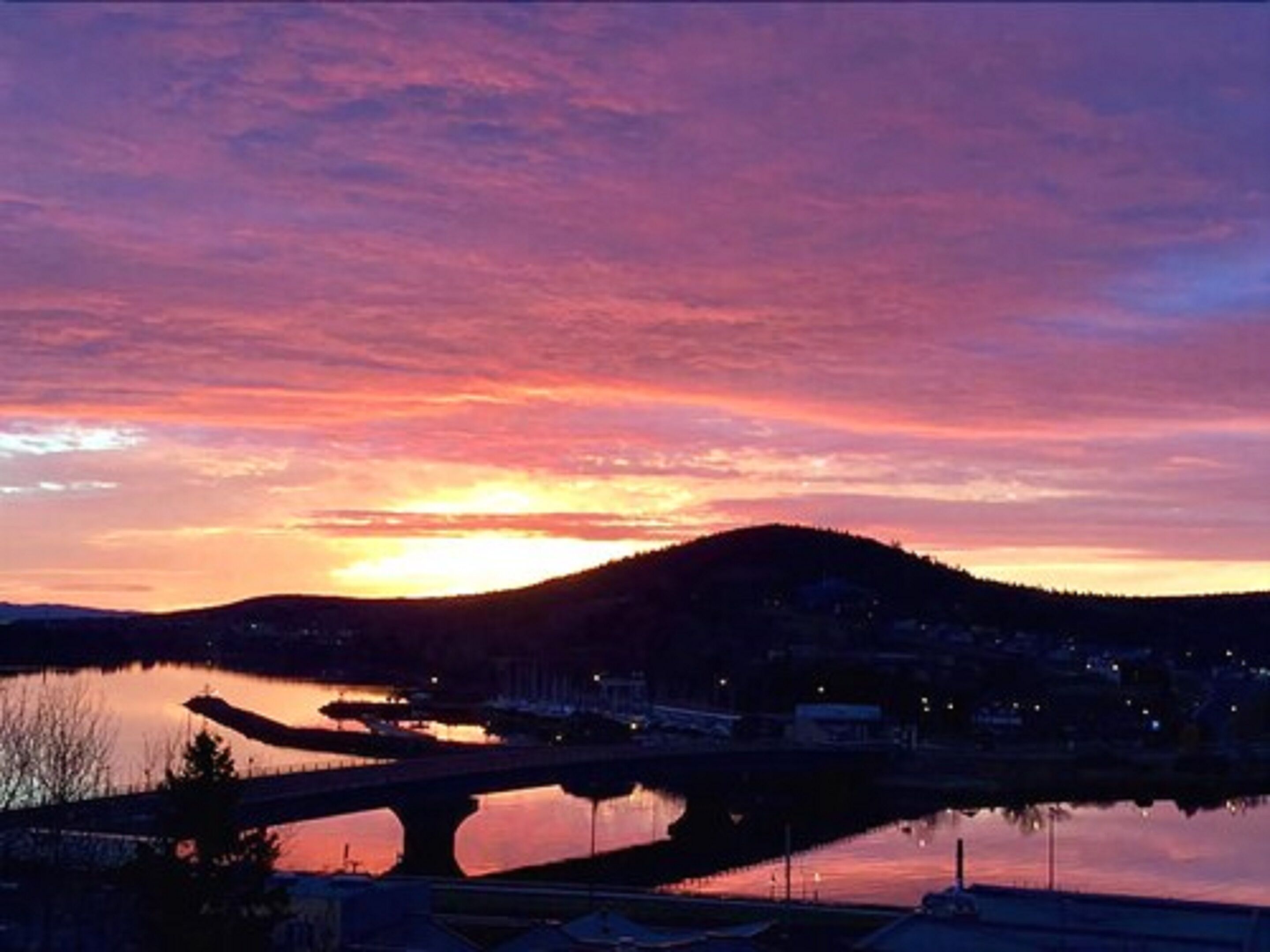 A sunset over a river with a bridge and a hill in the background.