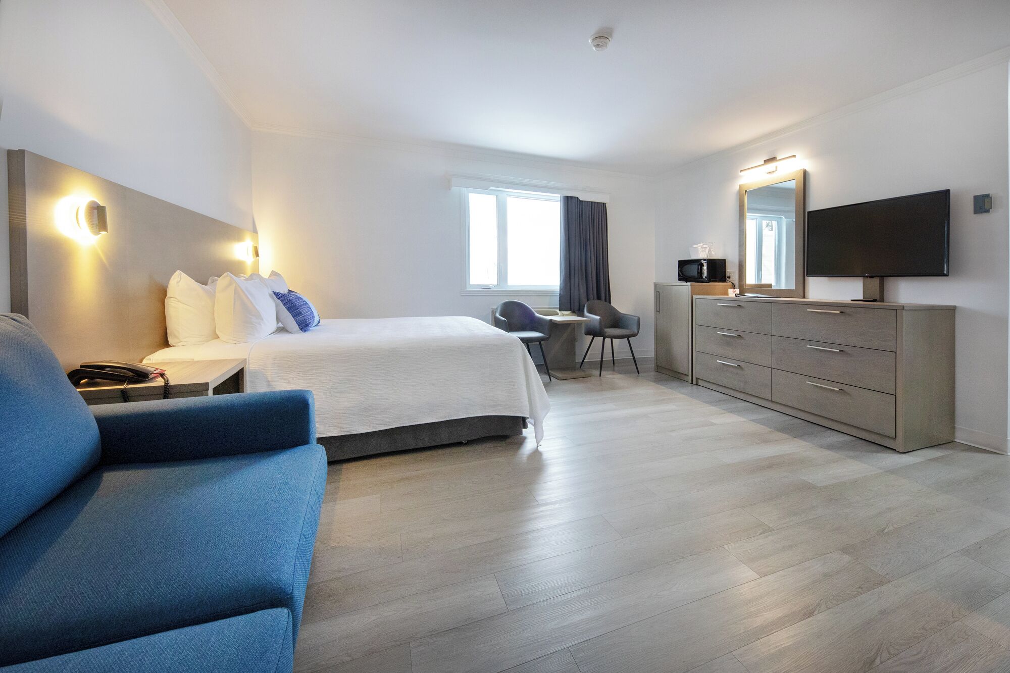 Ein modernes Hotelzimmer mit Bett, Schreibtisch, Stuhl, Kommode und Fernseher.