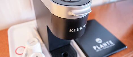 A Keurig coffee maker with a black base and a silver top, a black coffee pod holder, and a Keurig branded coffee pod.