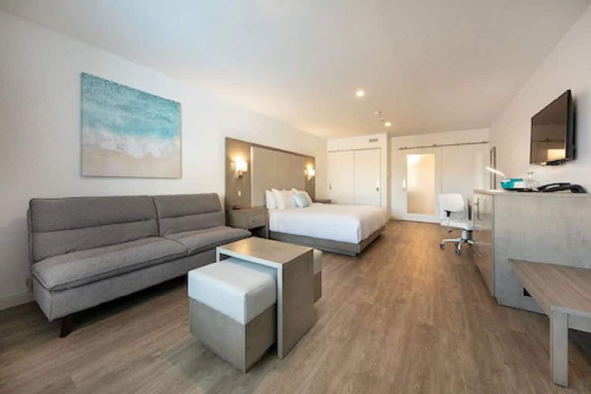 A modern hotel room with a sofa, a bed, a desk, and a small table.