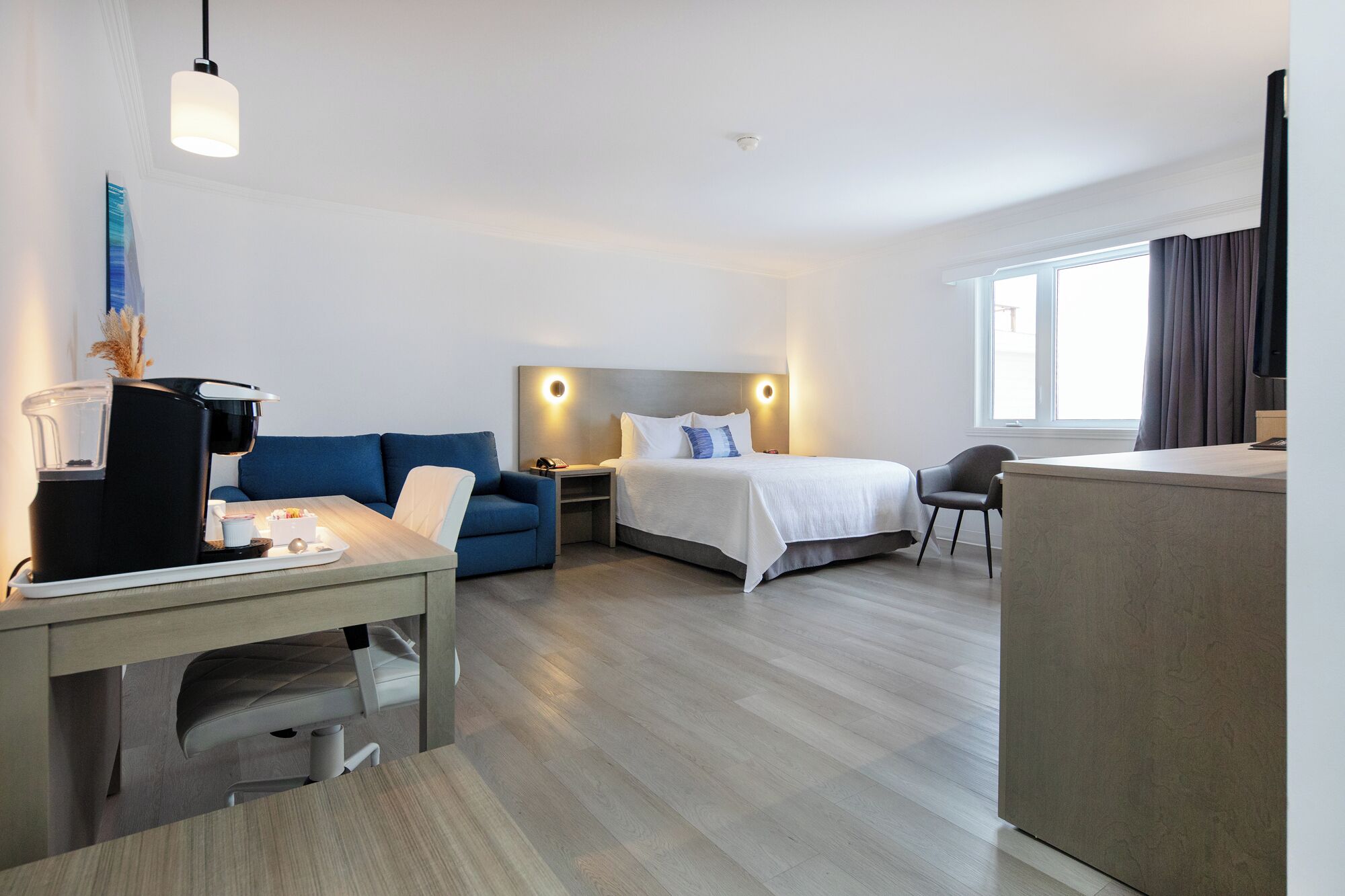 Une chambre d’hôtel avec un lit, un bureau doté d’une machine à café, un canapé bleu et une table de chevet.