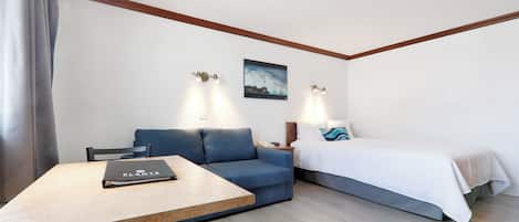 A hotel room with a bed, a blue sofa, a wooden table, and two wall-mounted lights.