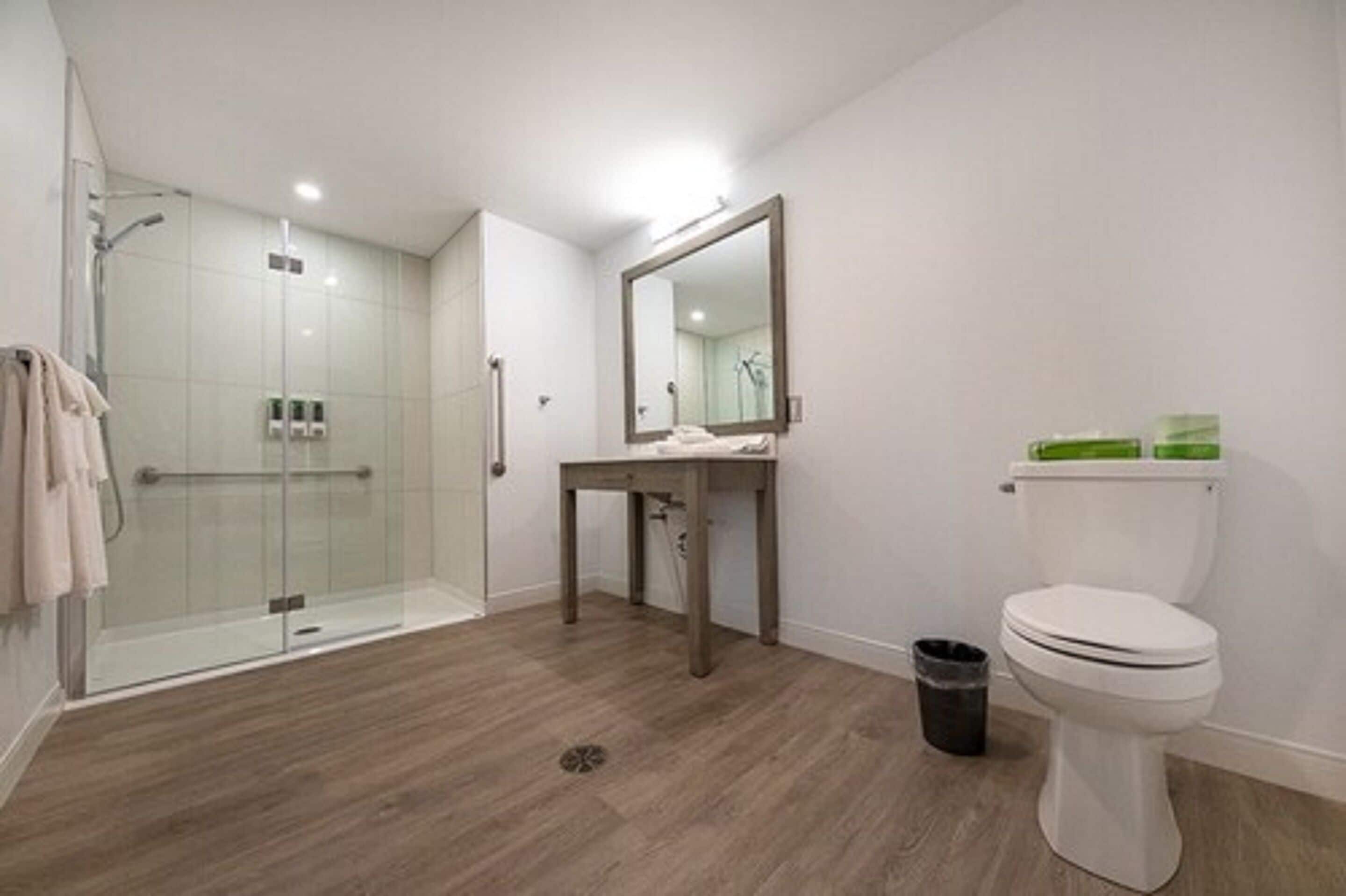 Un baño moderno con cabina de ducha de vidrio, inodoro blanco, tocador con espejo y un cubo de basura.