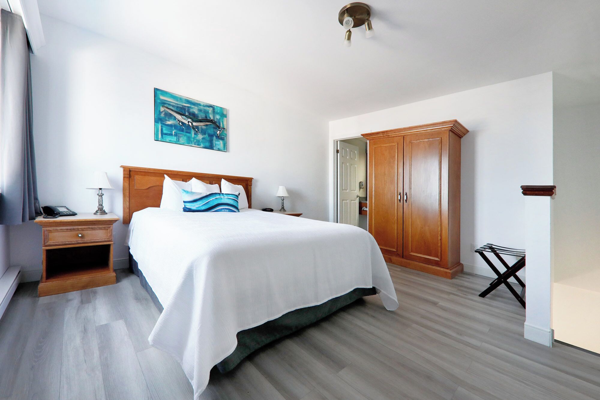 A hotel room with a bed, bedside tables, a wardrobe, and a painting on the wall.