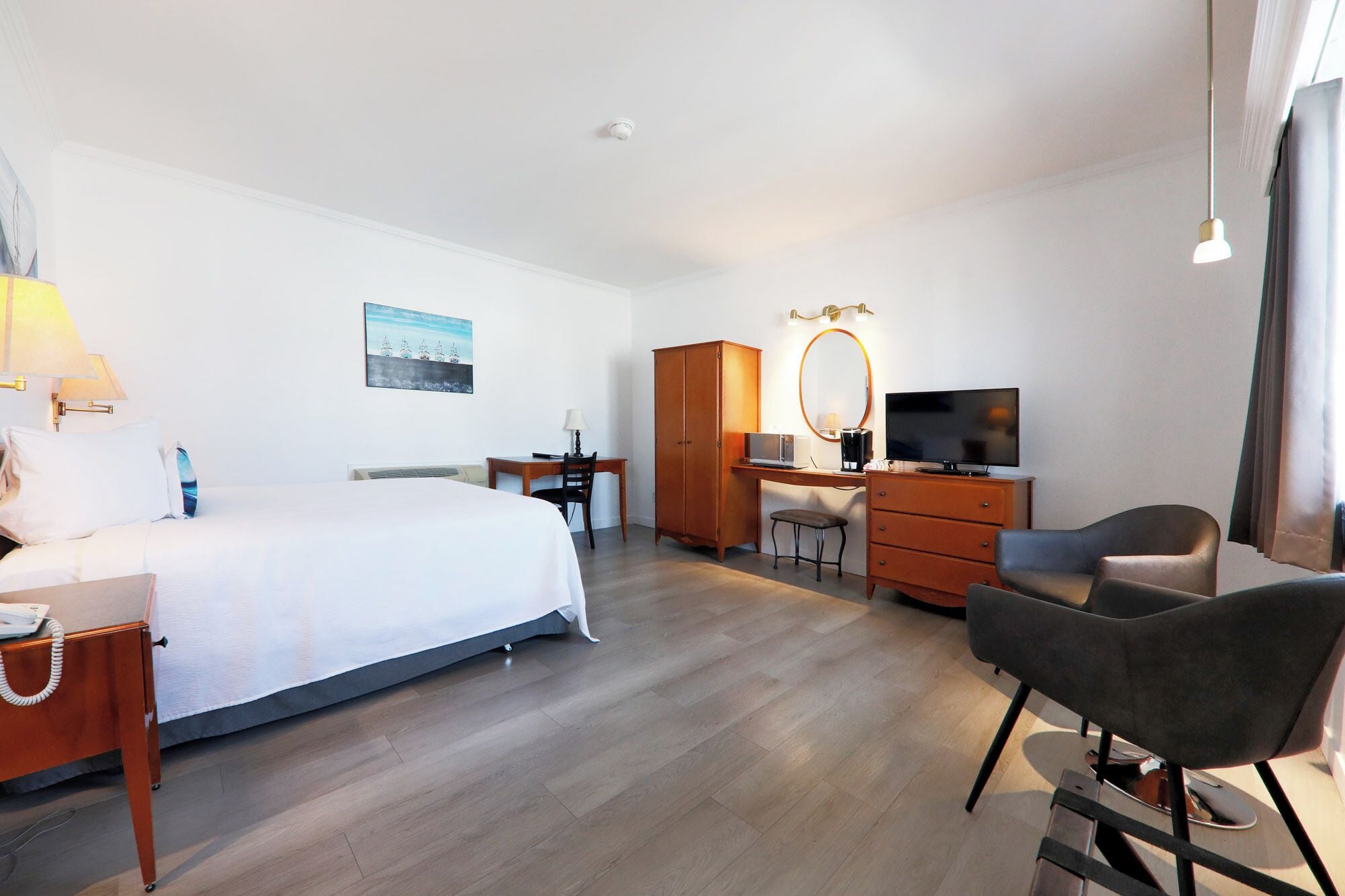 A hotel room with a bed, desk, chair, TV, wardrobe, and a painting on the wall.