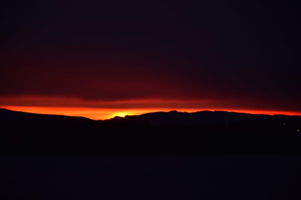 A silhouette of a mountain range against a dark sky with a red-orange glow near the horizon.