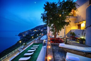 A rooftop terrace with sun loungers, a dining area with a table and chairs, and a view of the sea and hills. - La Casa del Melograno (Furore)