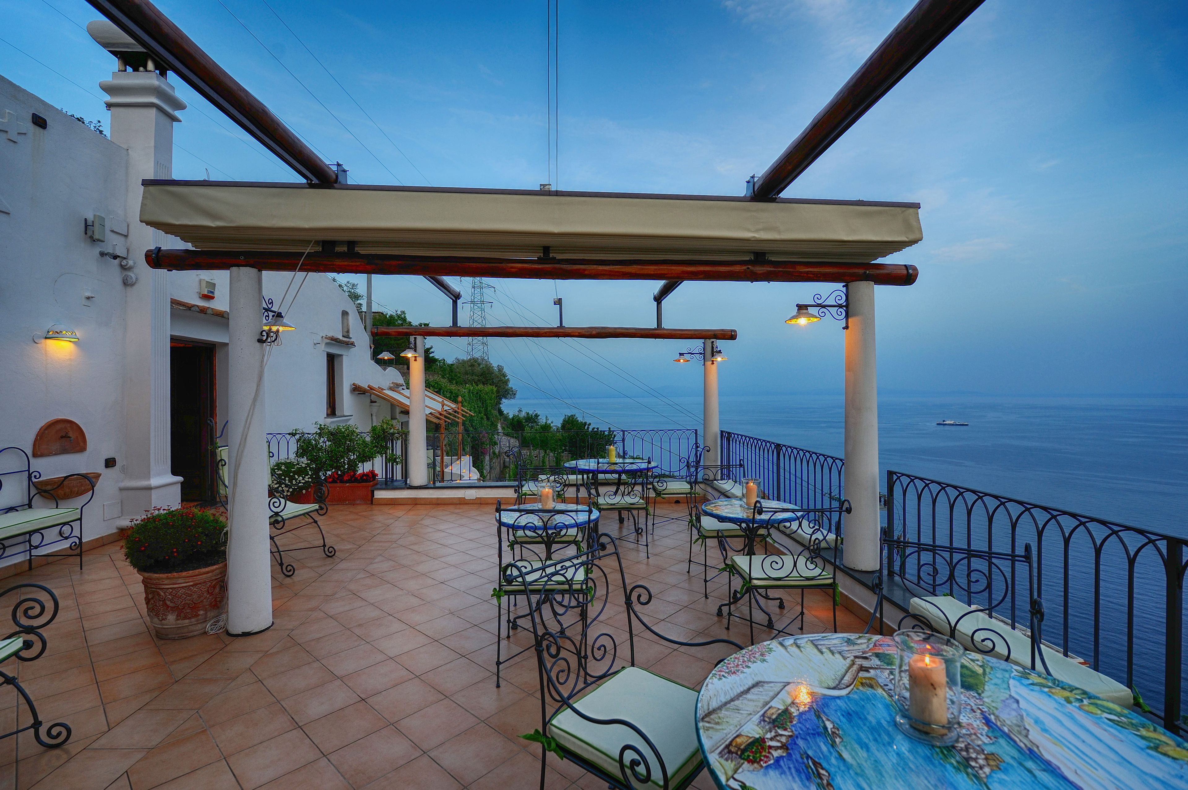 An outdoor patio with tables and chairs, a pergola, and a view of the sea.