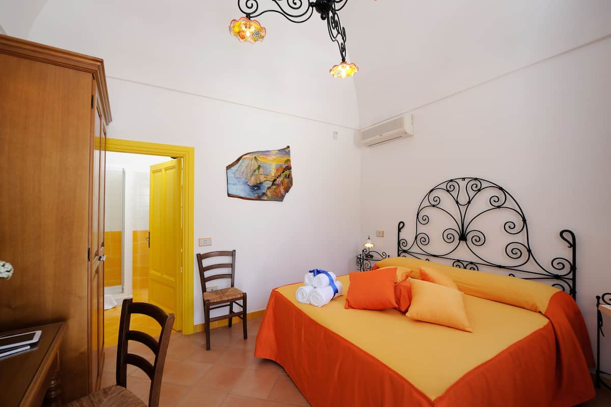 A bedroom with a bed, a chair, a desk, and a door leading to another room.