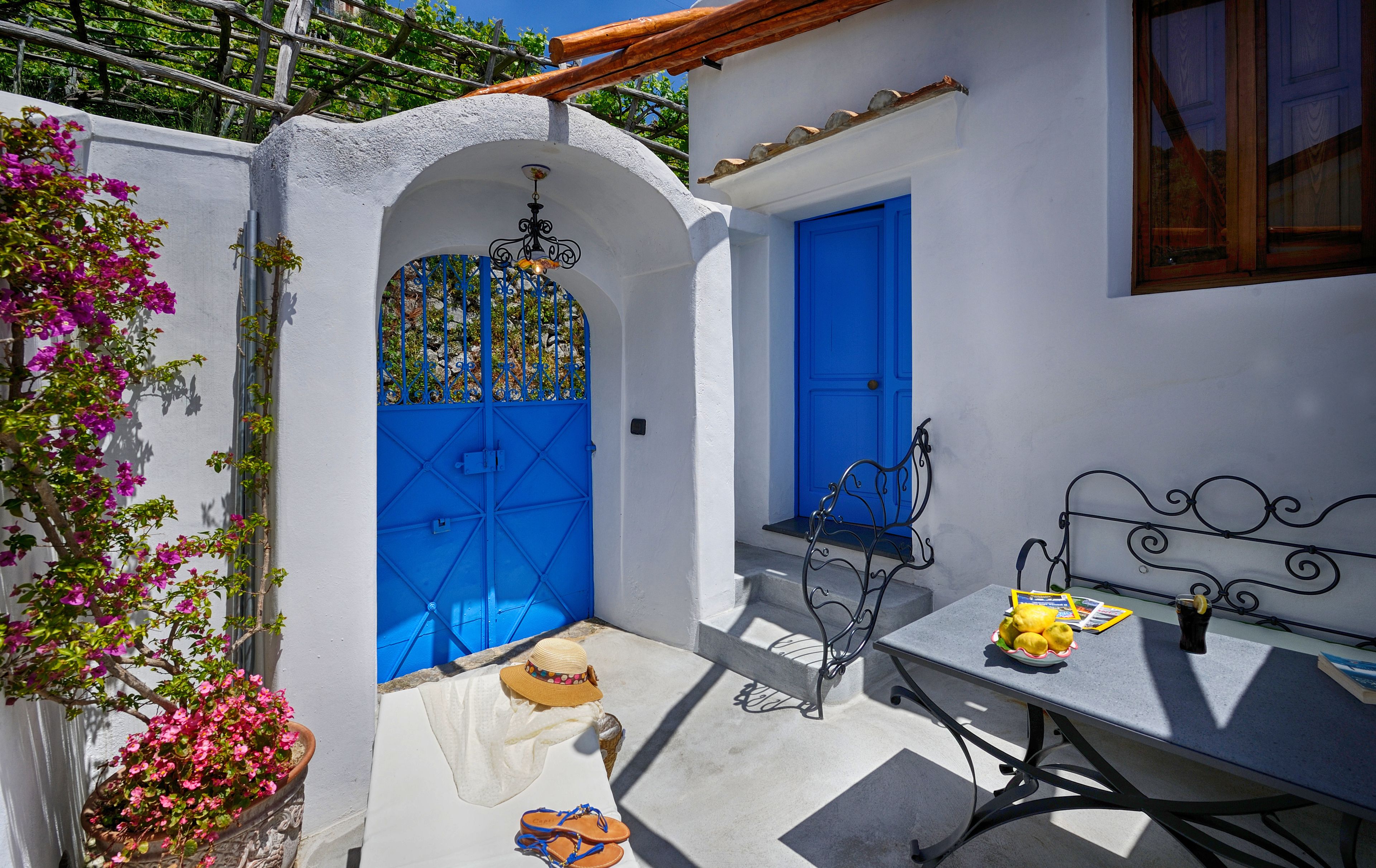 A courtyard with a blue door, a table with a basket of lemons, and a chair.