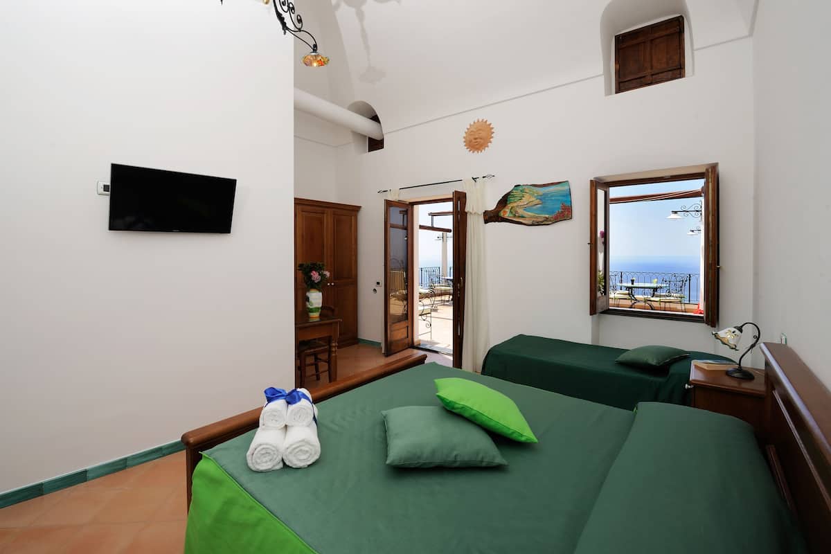 A hotel room with two beds, a TV, a painting, and a view of the sea.