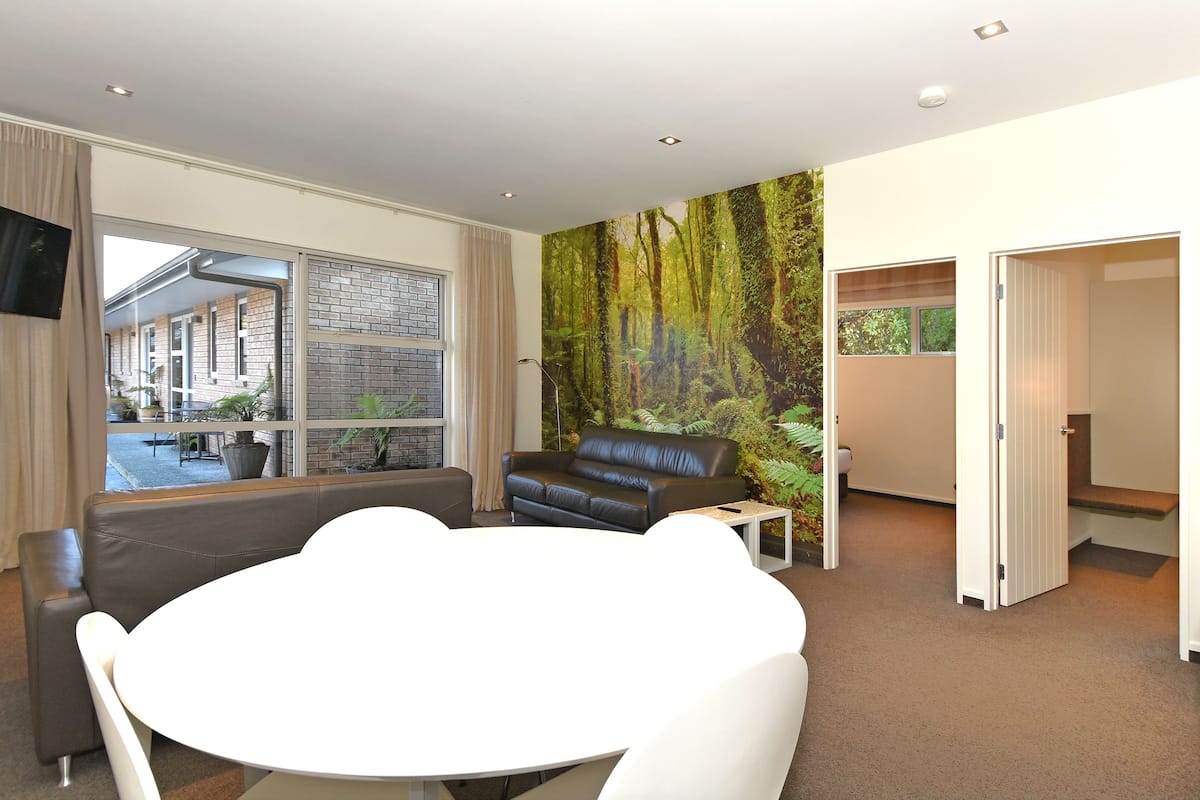 Ein modernes Wohnzimmer mit großem Fenster, einer schwarzen Ledersofa, einem weißen runden Tisch und einer Wandmalerei zum Thema Wald.