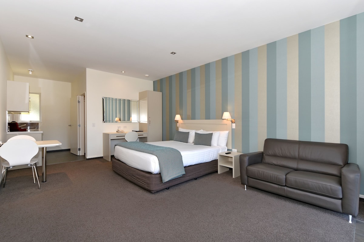 Ein modernes Hotelzimmer mit Bett, Schreibtisch, Stuhl, Sofa und einer gestreiften Wand.