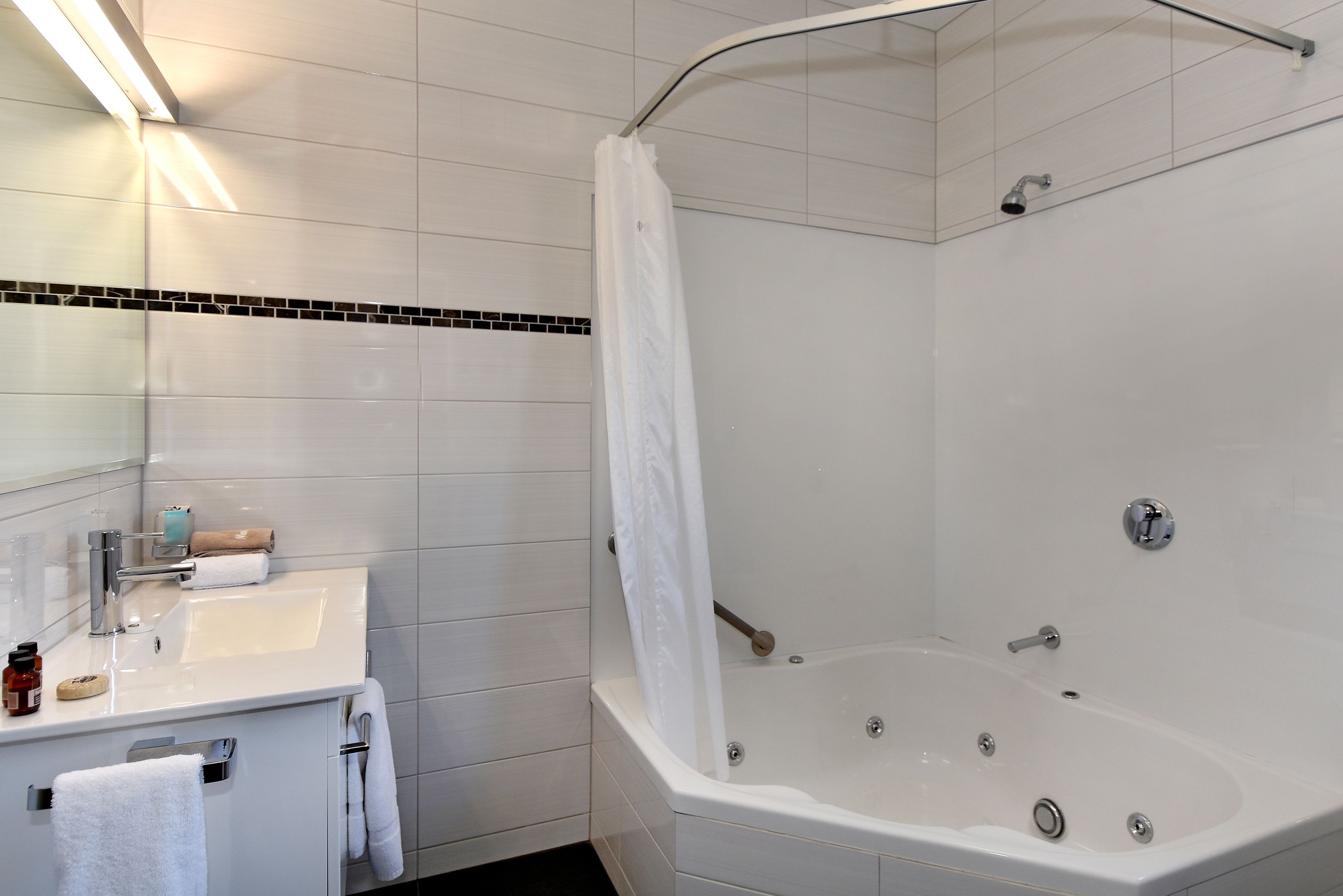 Un baño moderno con lavamanos, espejo y bañera blancos.