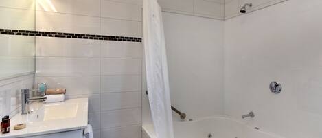 Un baño moderno con lavamanos, espejo y bañera blancos.
