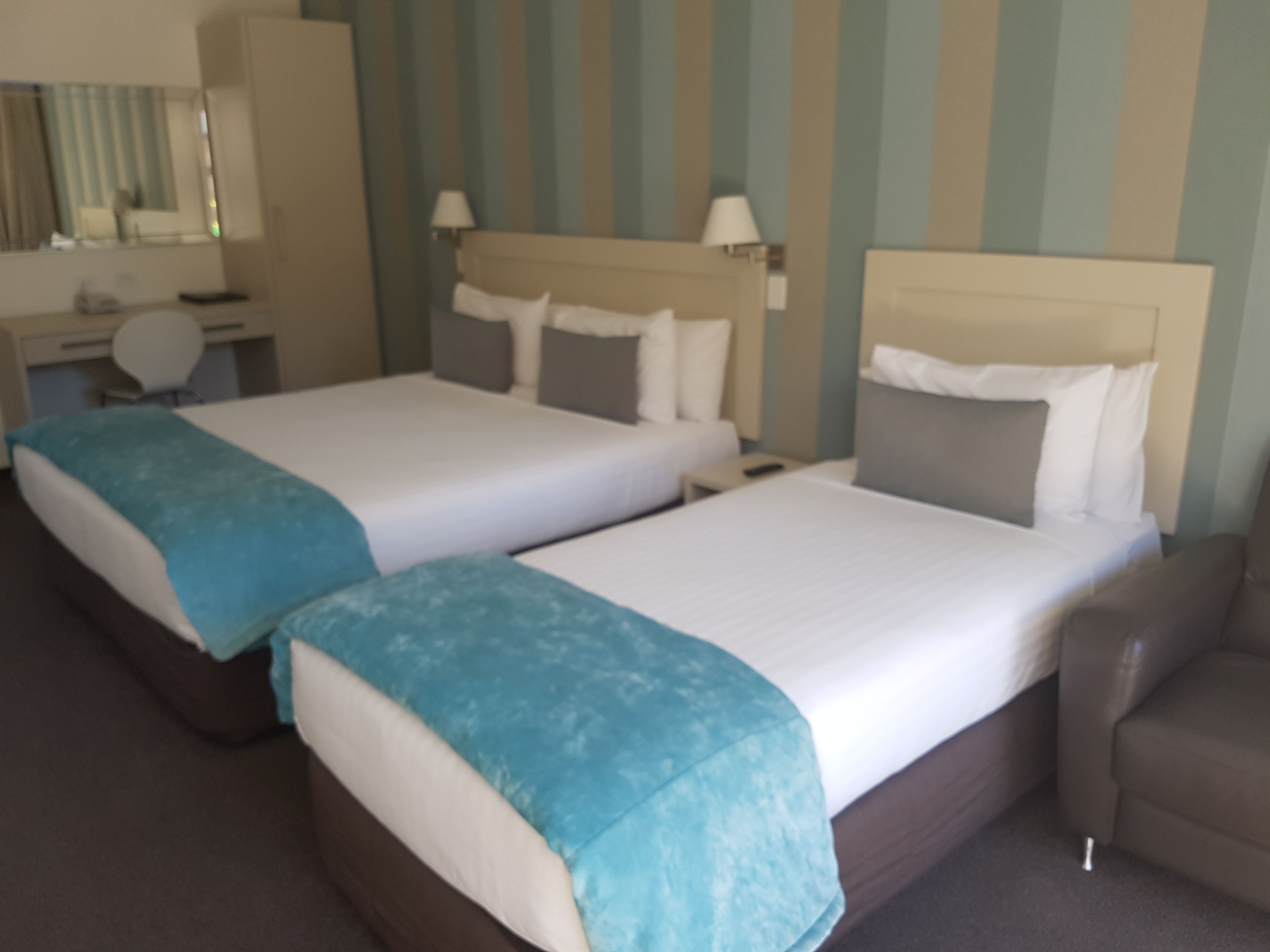 A hotel room with two beds, a desk, a chair, and a mirror.