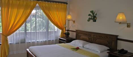 A hotel room with a large bed, a nightstand, a lamp, and a window with yellow curtains.