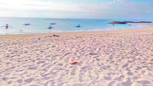 Una playa arenosa con barcos en el agua y un promontorio rocoso a lo lejos.