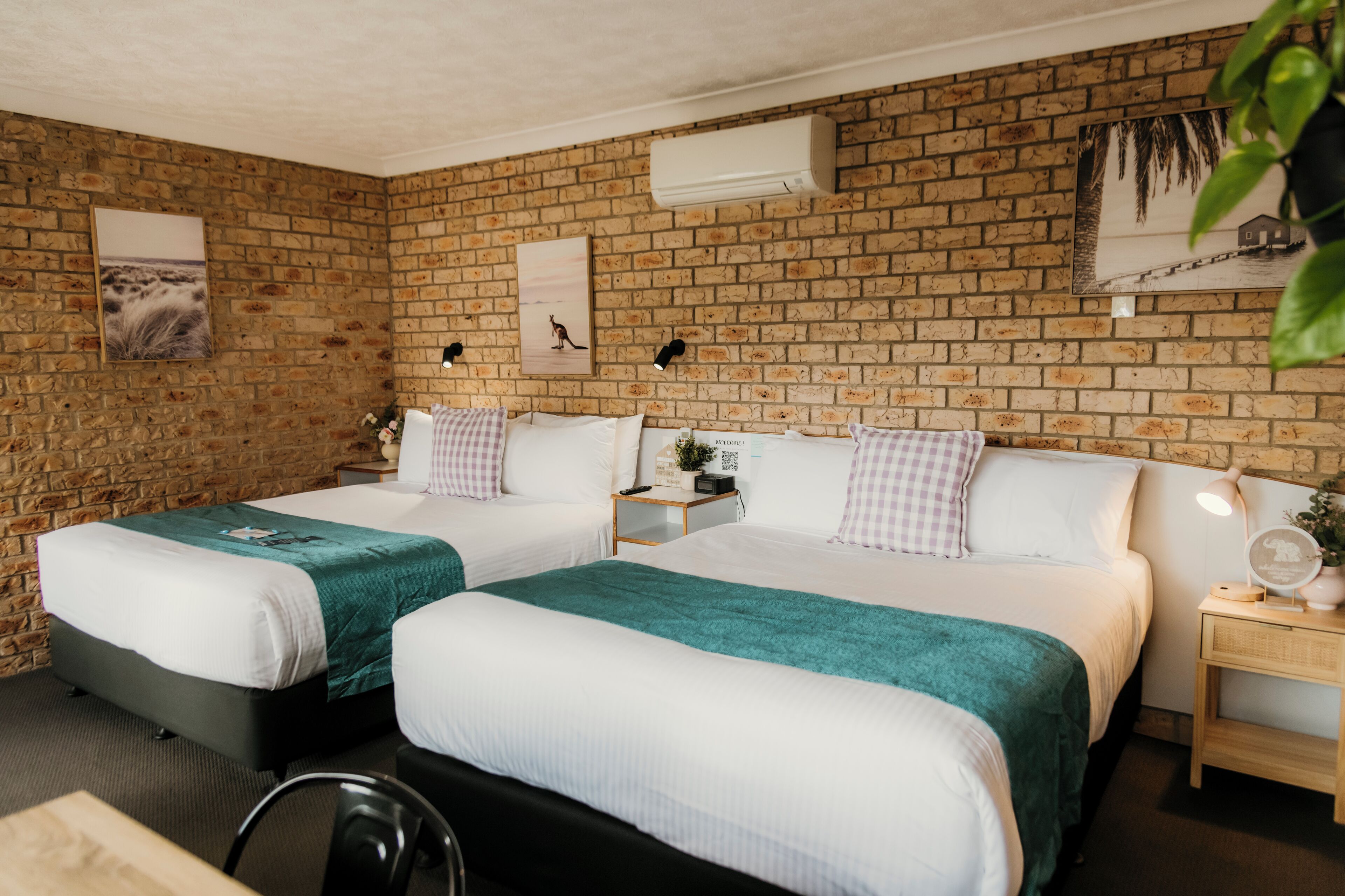 A hotel room with two beds, a brick wall, and a small bedside table with a lamp.
