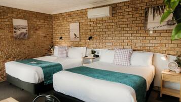A hotel room with two beds, a brick wall, and a small bedside table with a lamp.