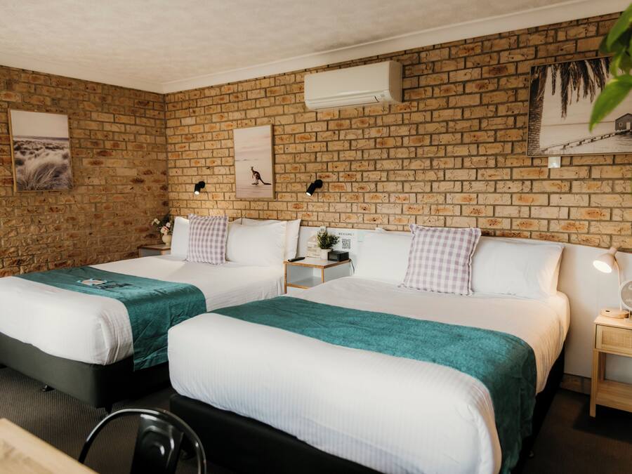 A hotel room with two beds, a brick wall, and a small bedside table with a lamp.