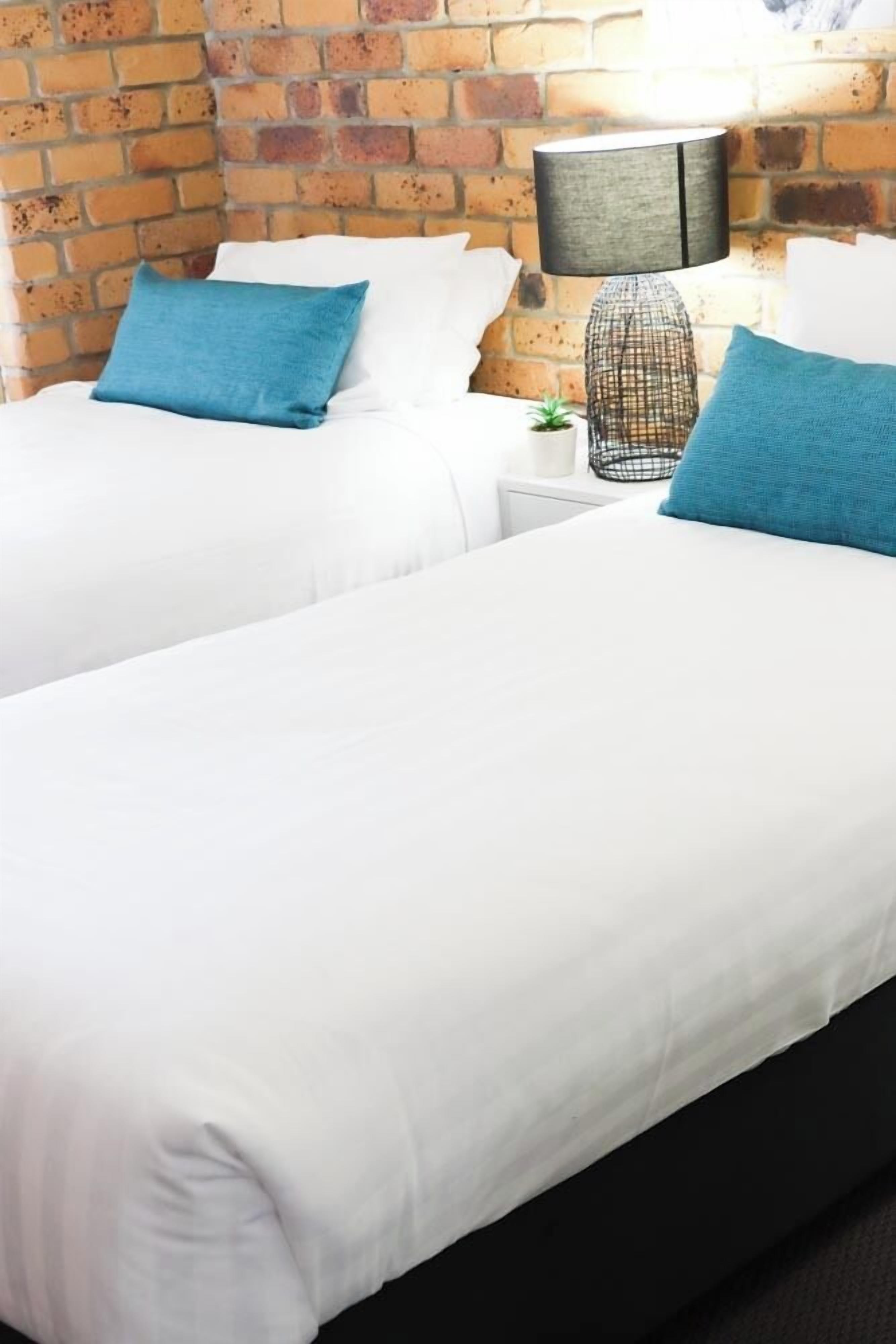 A hotel room with two beds, white bedding, and a brick wall.